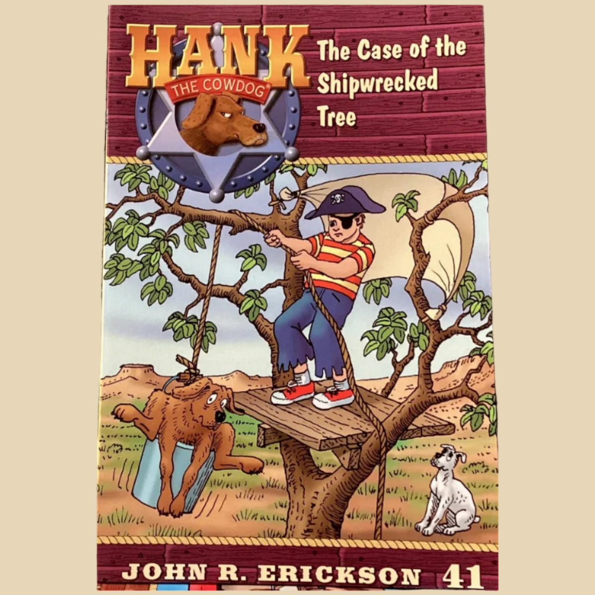Book titled 'Hank the Cowdog: The Case of the Shipwrecked Tree' by John R. Erickson on a table against a dark wall.