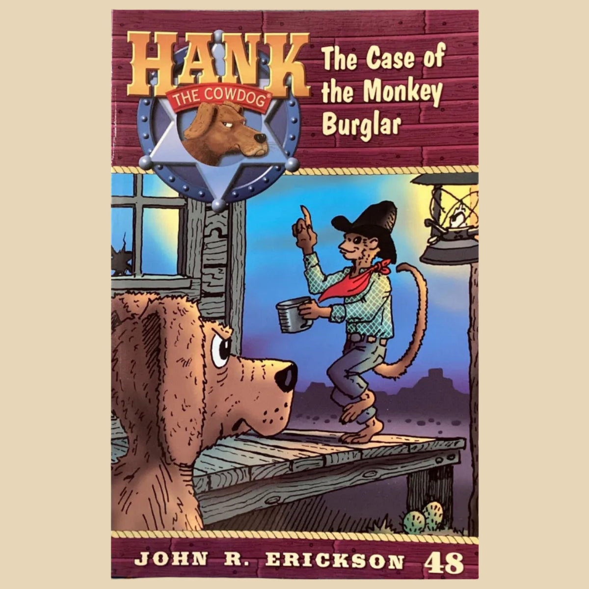 Book titled 'Hank the Cowdog: The Case of the Monkey Burglar' by John R. Erickson on a gray wall.