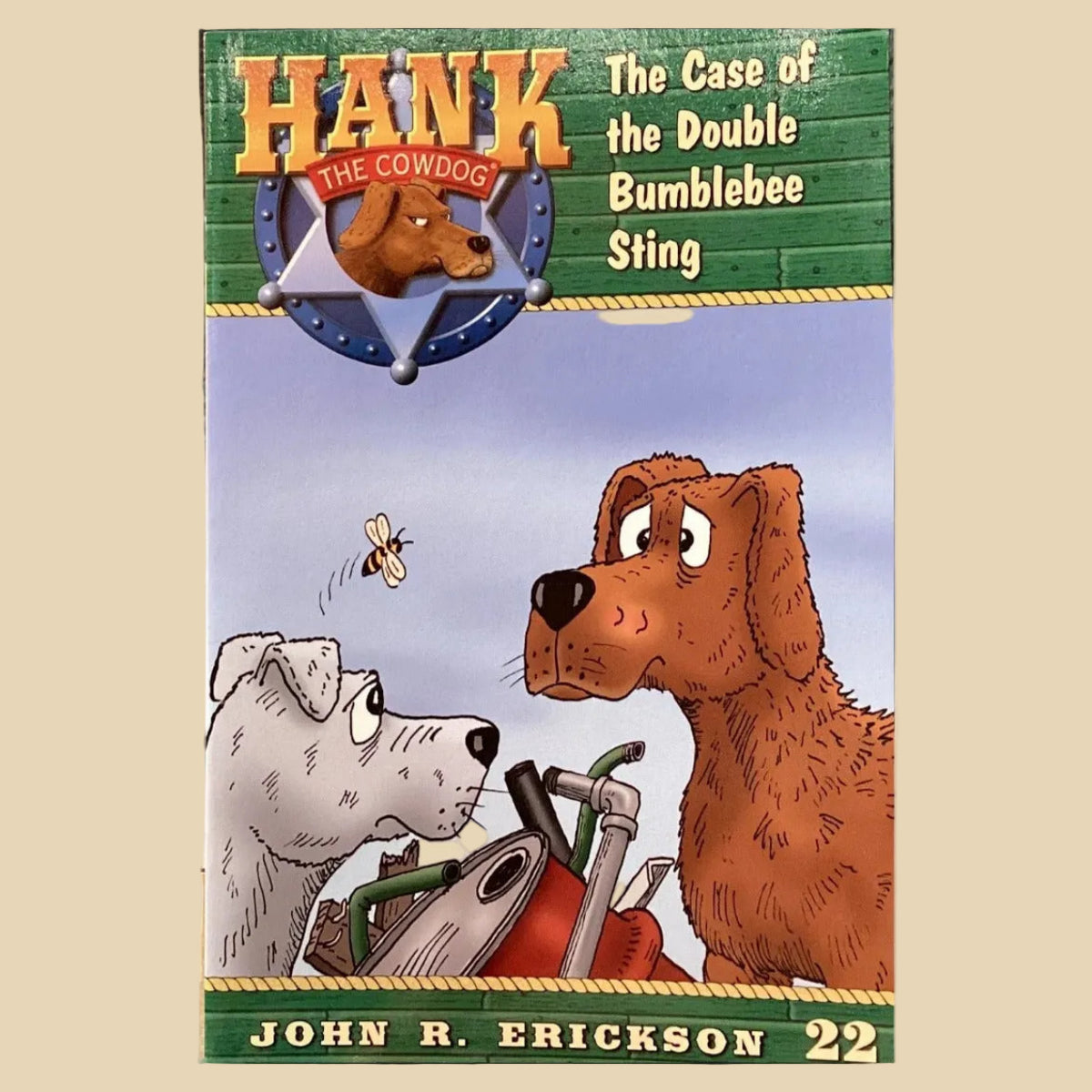 Book titled 'Hank the Cowdog: The Case of the Double Bumblebee Sting' by John R. Erickson on a surface with a gray wall background.