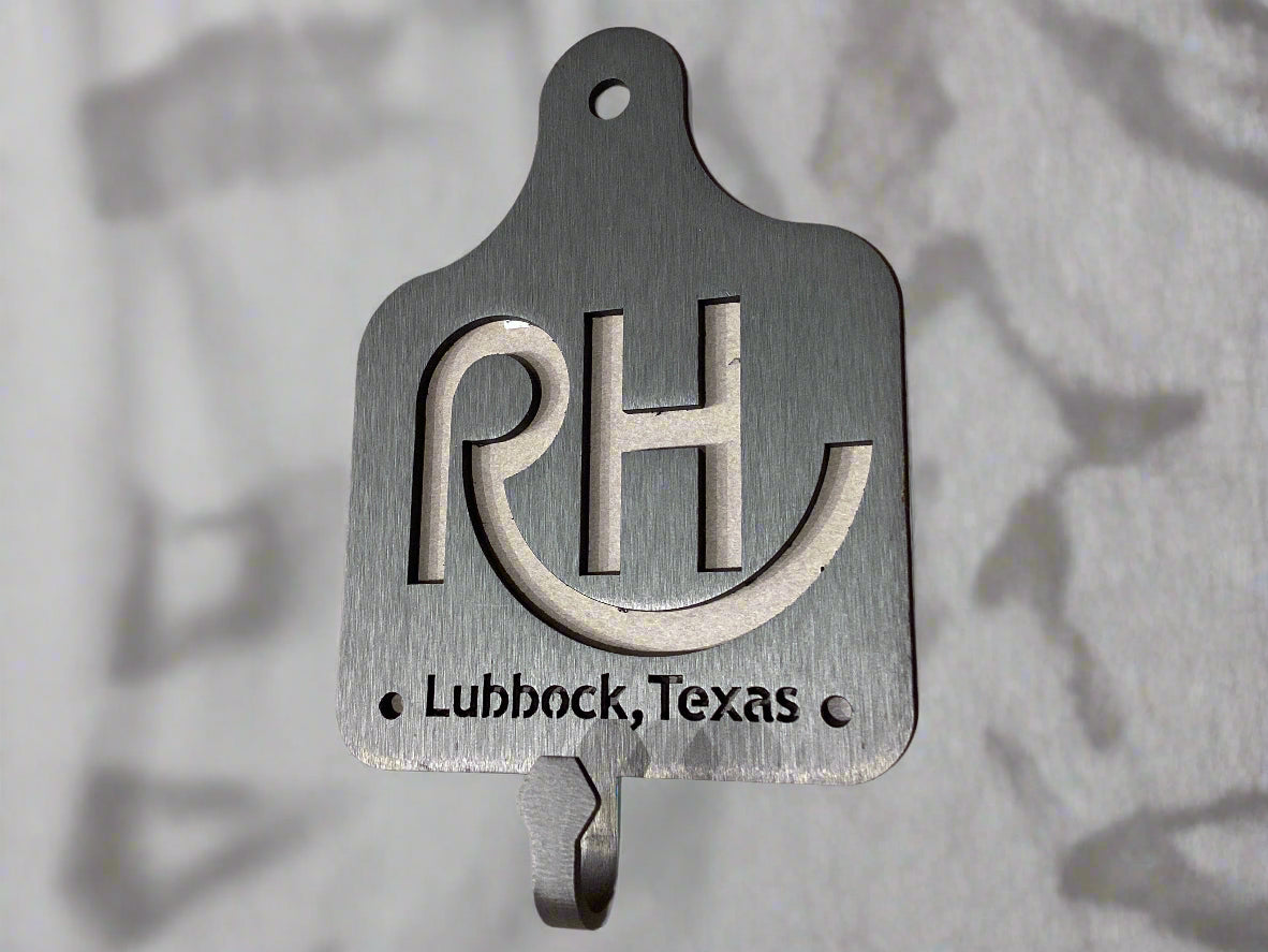 Metal wall hook with 'RH' and 'Lubbock, Texas' text on a beige background
