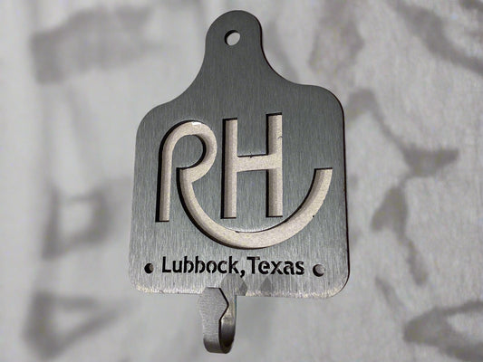 Metal wall hook with 'RH' and 'Lubbock, Texas' text on a beige background