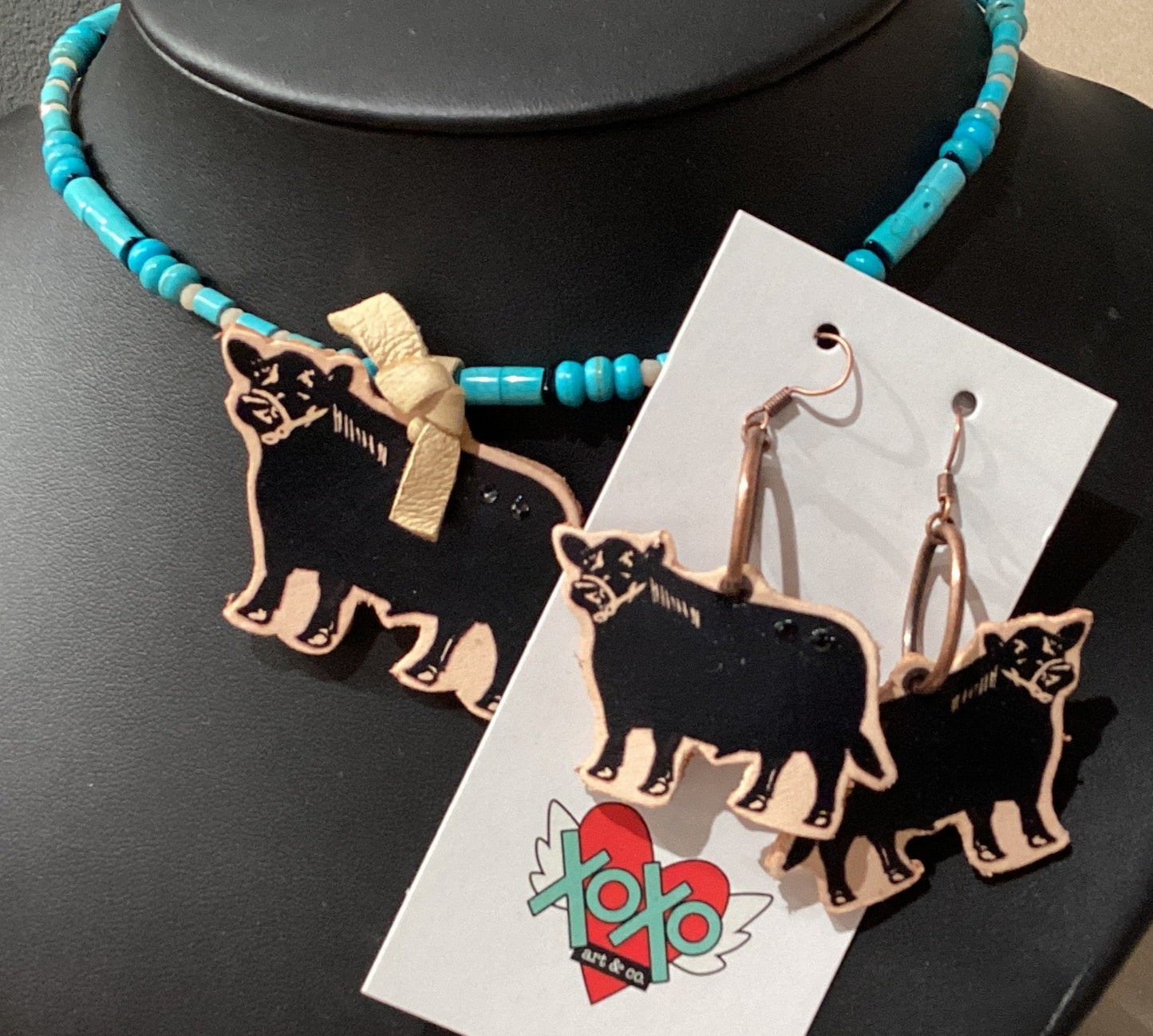 Jewelry set with necklace and earrings featuring animal designs on a black stand.