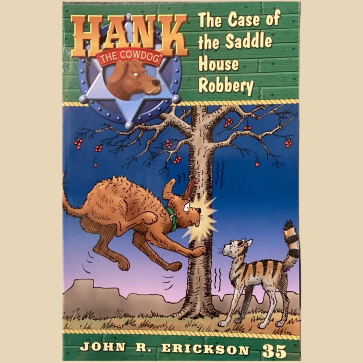 Book cover of 'Hank the Cowdog: The Case of the Saddle House Robbery' by John R. Erickson on a gray surface.