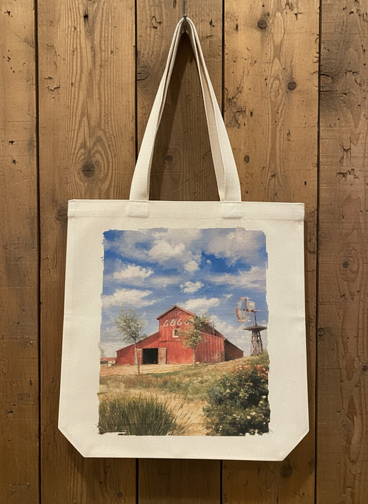 Tote bag with a red barn design hanging on a wooden cabinet.