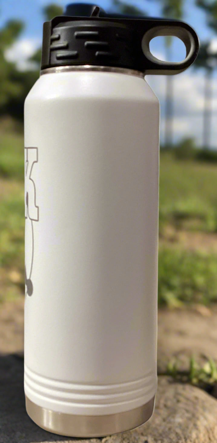 White insulated water bottle with black lid on a surface with a plant and book in the background.