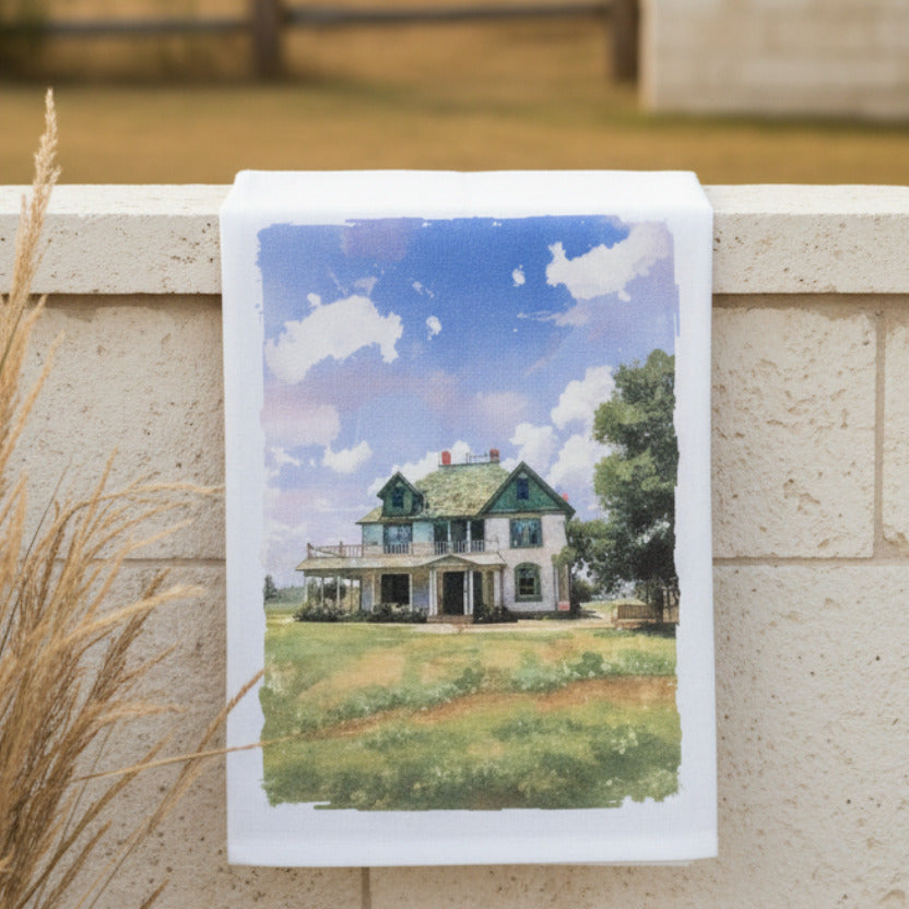 Towel with a printed design of a house and sky hanging on a wall.