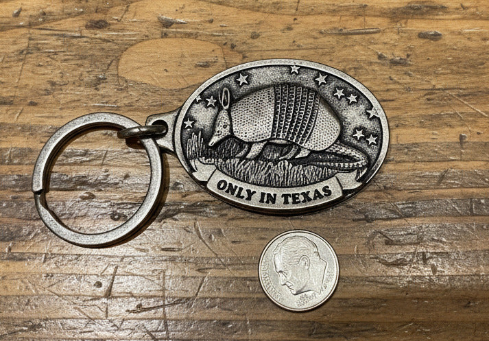 Metal keychain with armadillo design and 'Only in Texas' text on a textured surface.