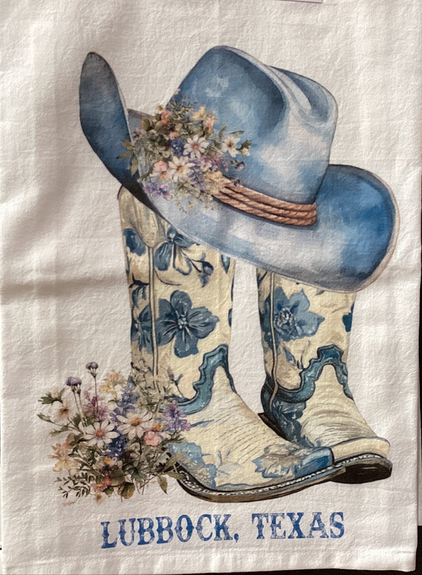 Decorative towel with cowboy boots and hat design, featuring 'Lubbock, Texas' text, on a gray wall.