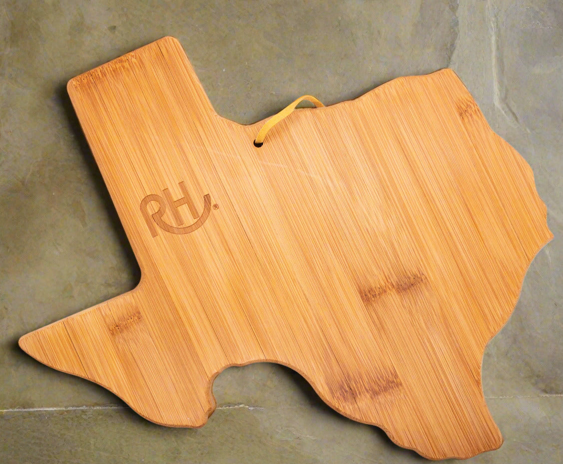A bamboo cutting board in the shape of the state of Texas, with a branded logo on the top surface and a hanging loop.