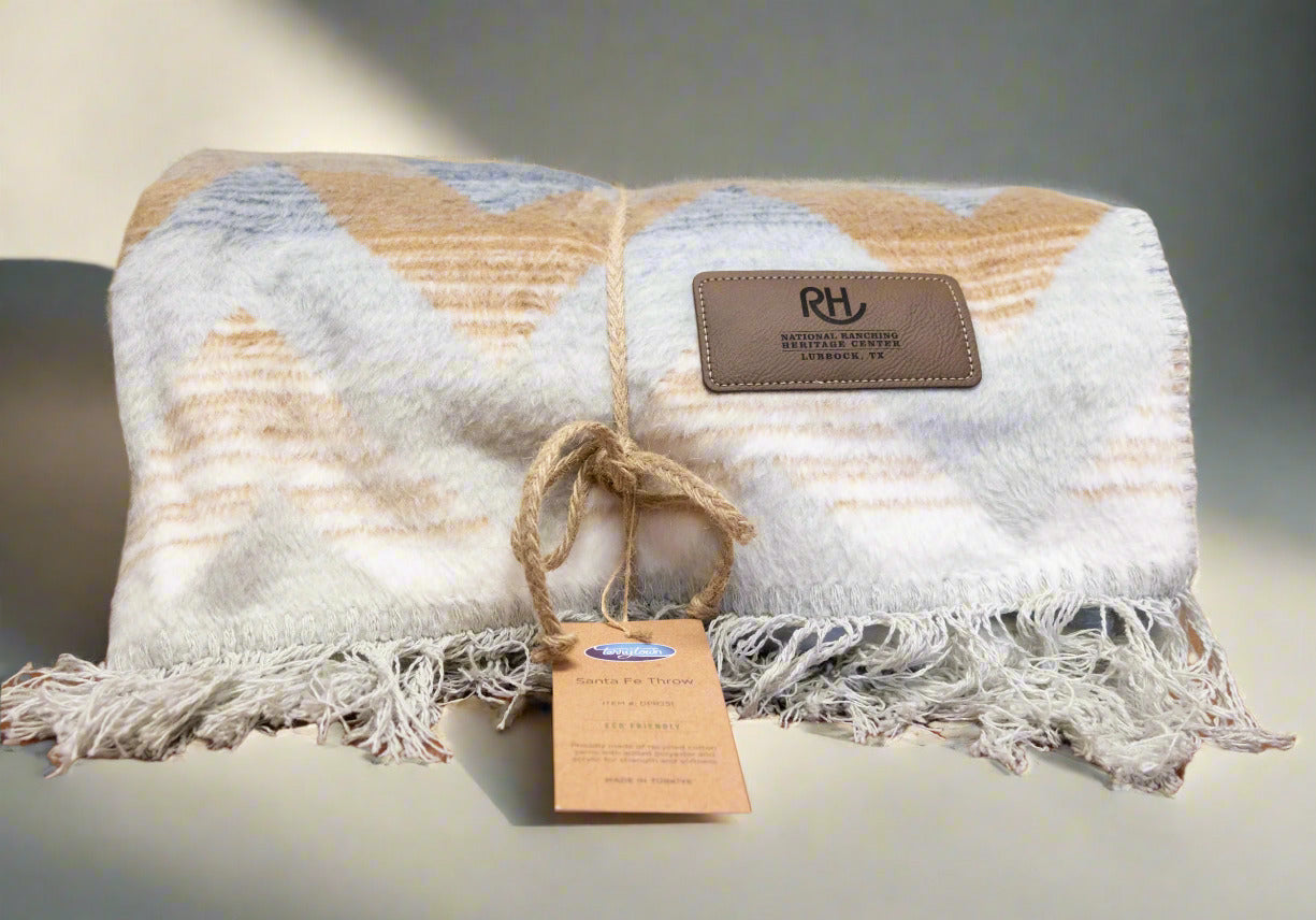 A folded blanket with a striped pattern, predominantly beige and white, with a fringe and a brand tag that reads 'RH'.