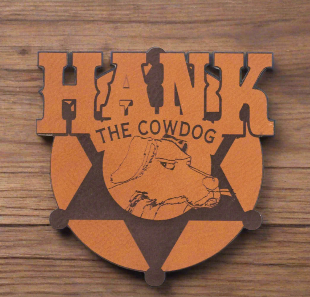 A brown leather magnet with the text 'HANK THE COWDOG' and an illustration of a cow.