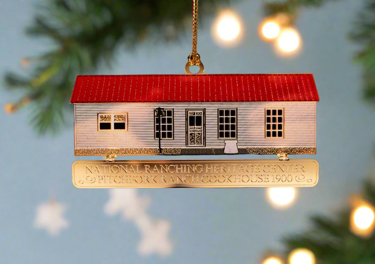 A metal cookhouse ornament with a red roof and silver body, hanging from a string.