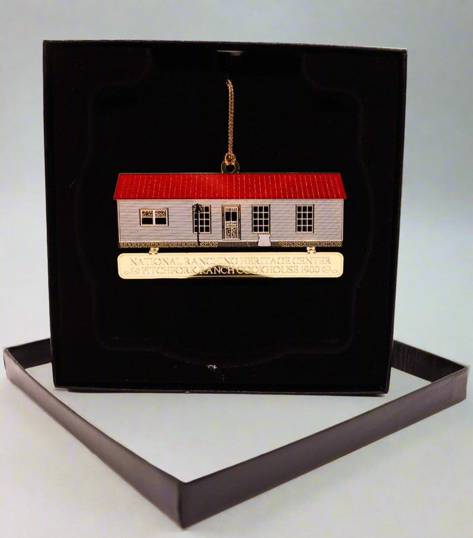 Decorative house ornament with red roof and gold accents on a black stand against a white background