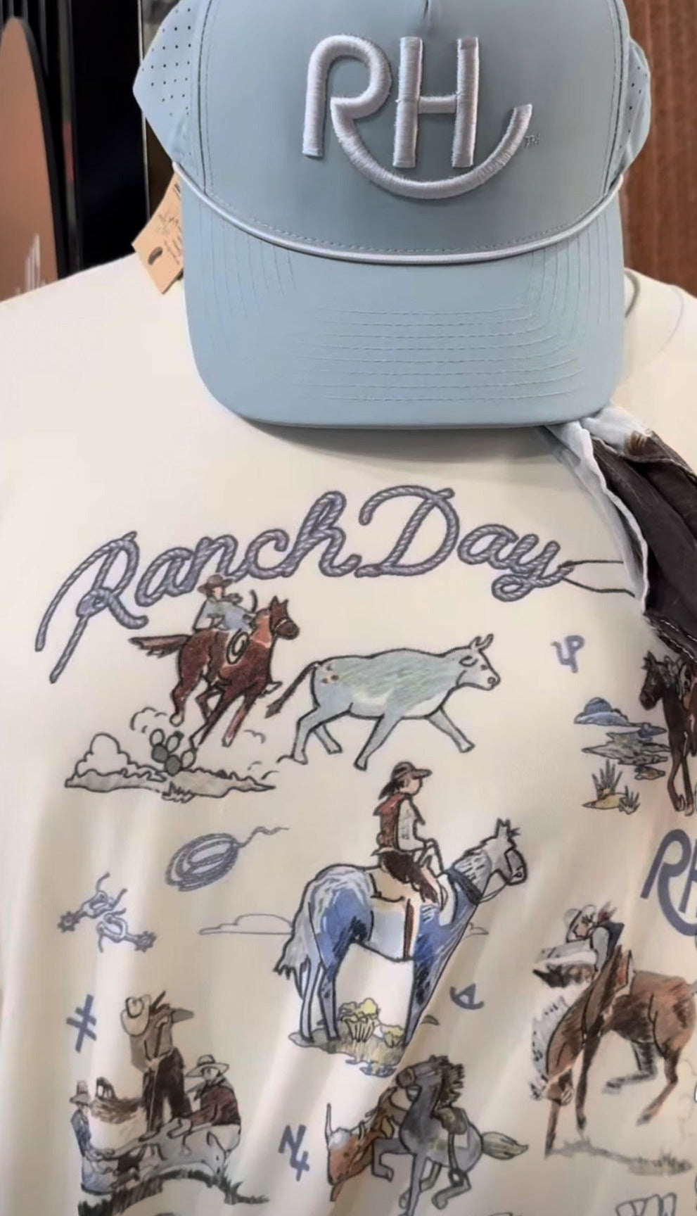 Light blue cap with 'RH' on a person wearing a 'Ranch Day' shirt with cowboy graphics.