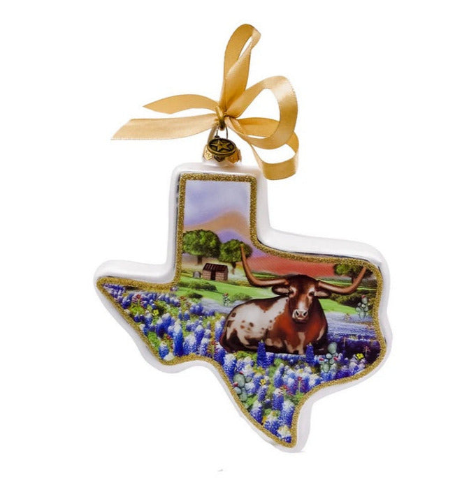 Decorative ornament shaped like the state of Texas with a cow and bluebonnets on a white background.