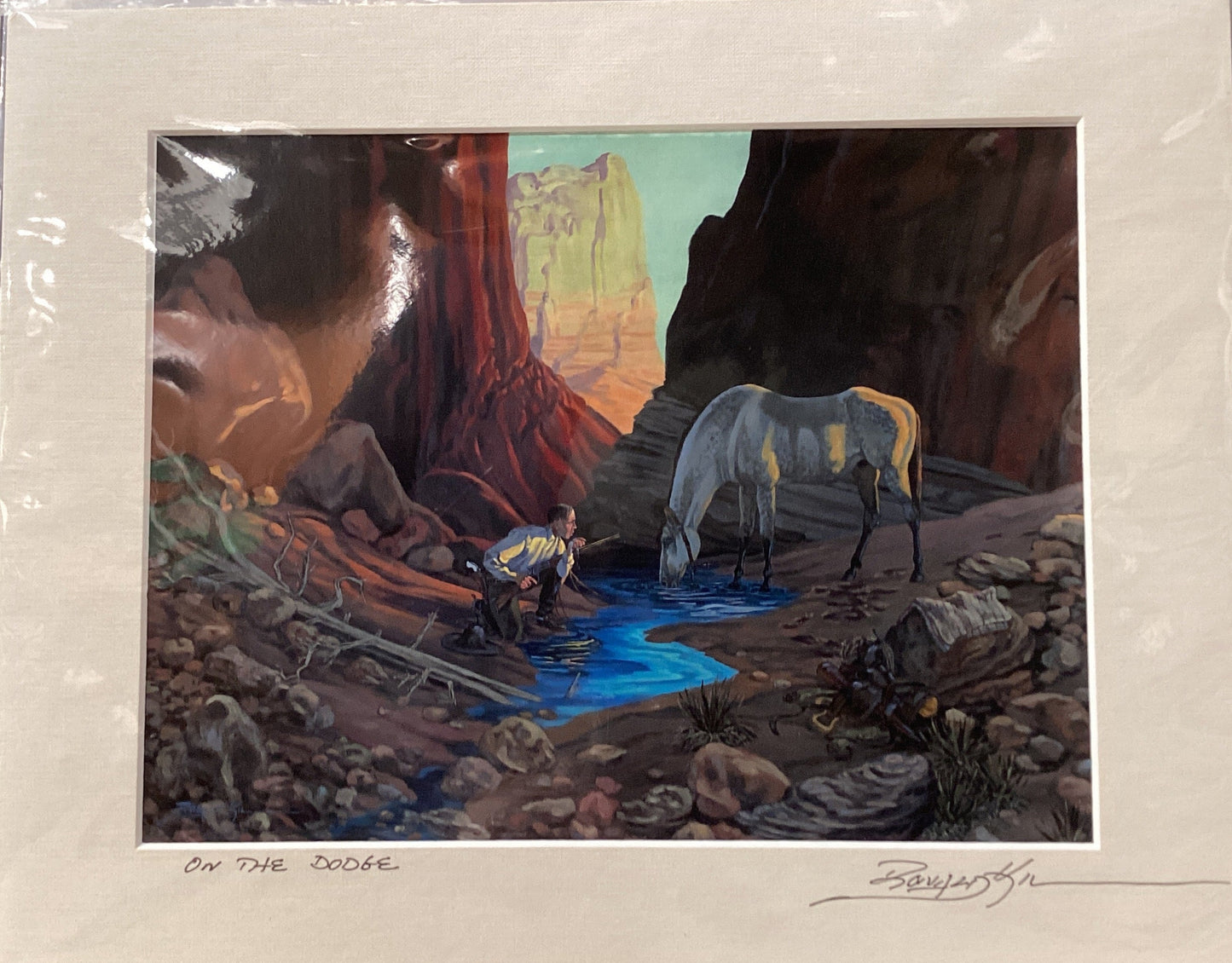 Framed artwork of a desert landscape with a horse and person by a stream.