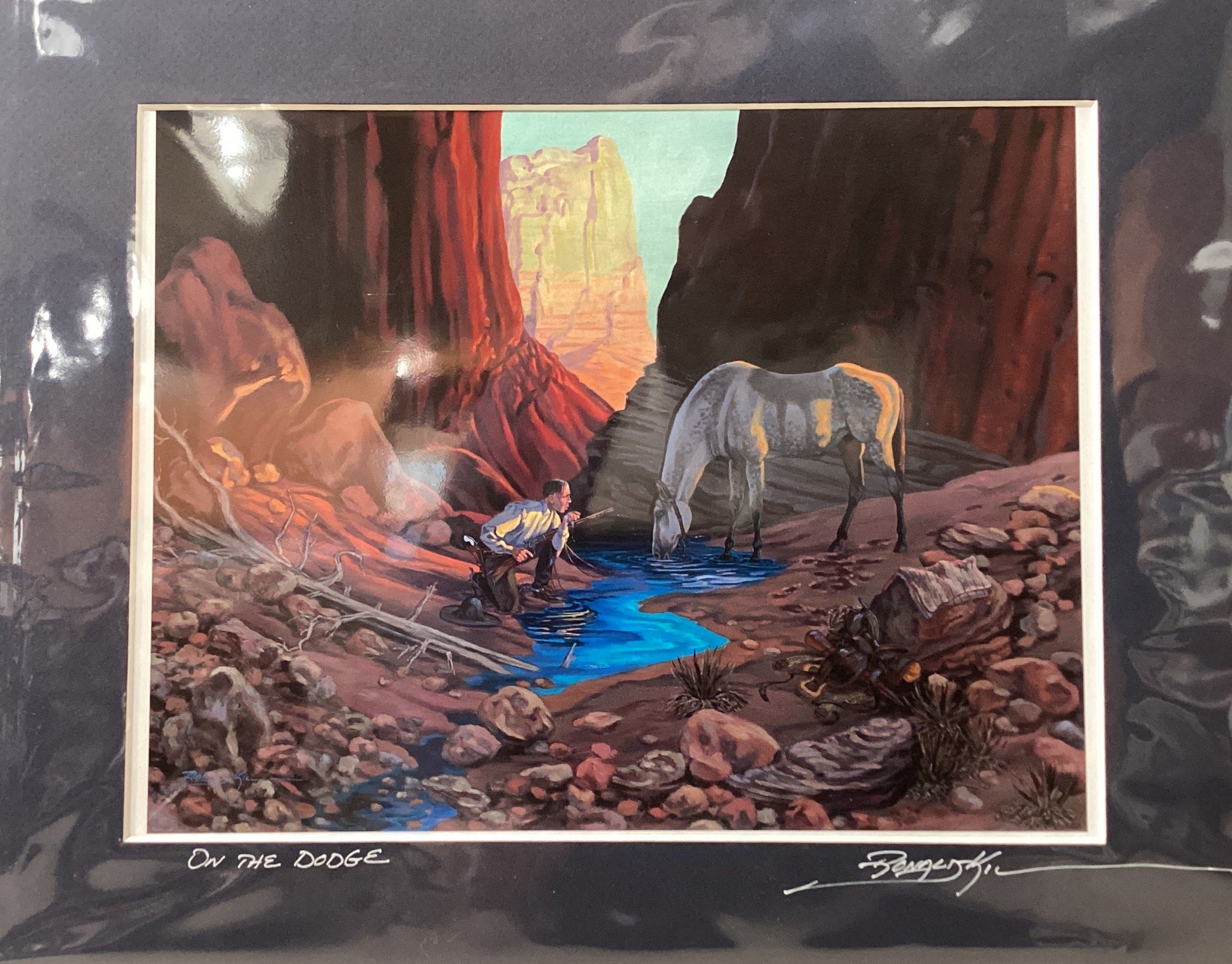 Framed artwork of a desert scene with a horse and person by a water source.