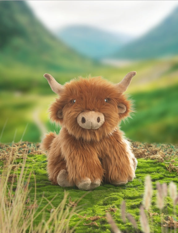 Plush toy Highland cow in a natural setting with green hills and sky.
