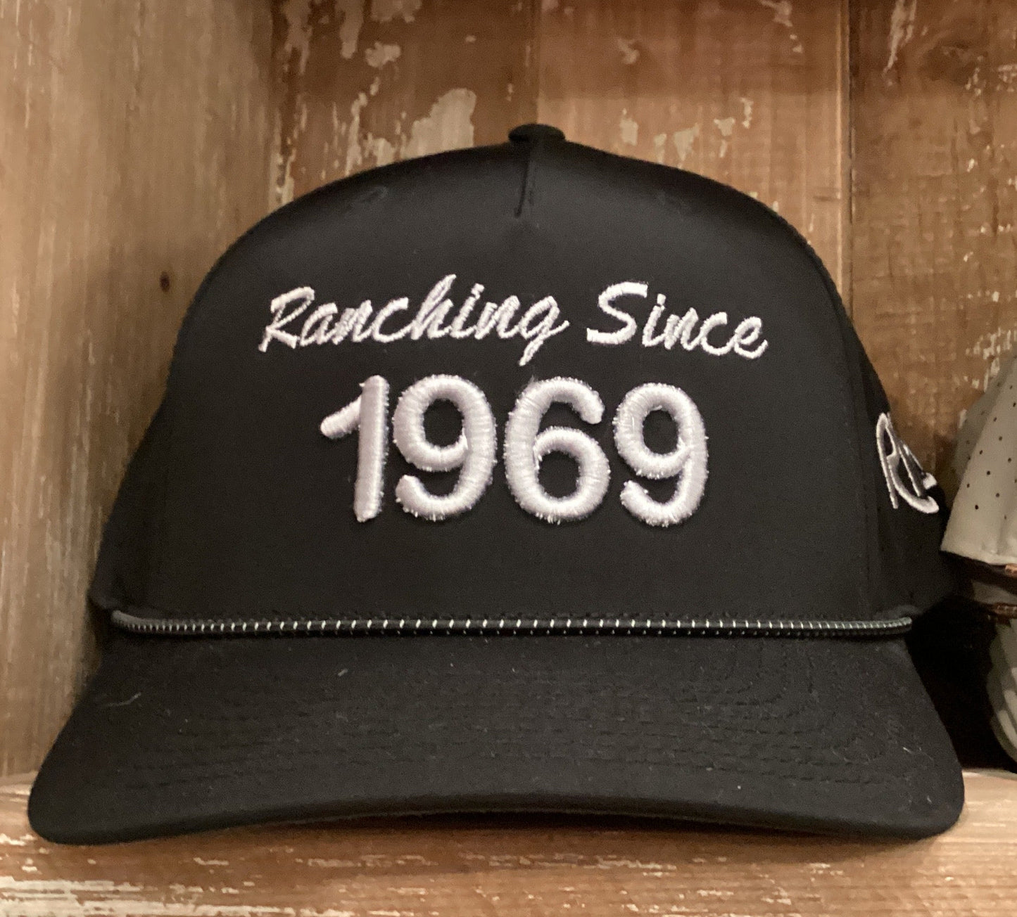 Black cap with 'Ranching Since 1969' text on a wooden shelf
