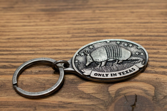 Metal keychain with armadillo design and 'Only in Texas' text on a light gray surface.