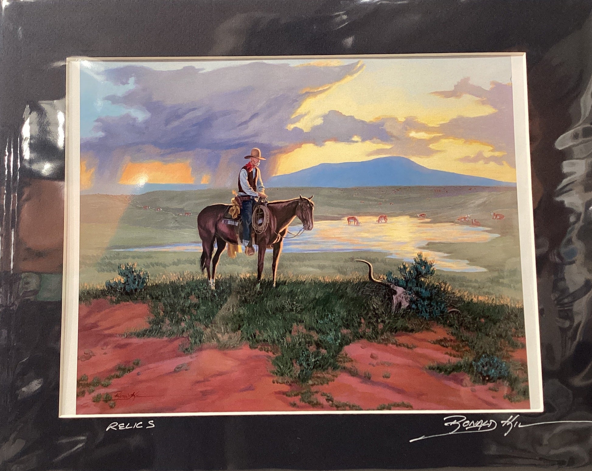 Framed artwork of a landscape with a person on horseback, mountains, and sunset.