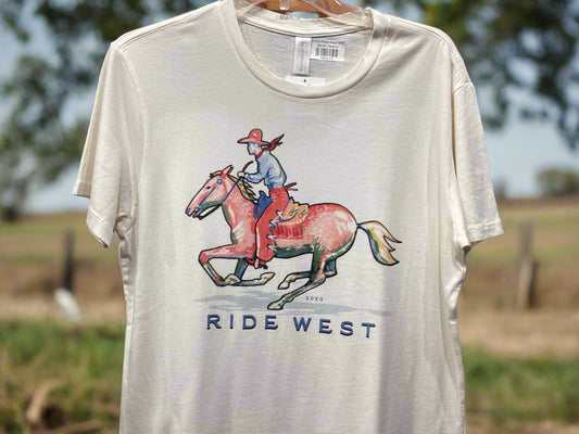 Beige t-shirt with a graphic of a person riding a horse and 'RIDE WEST' text, hanging against a gray wall.