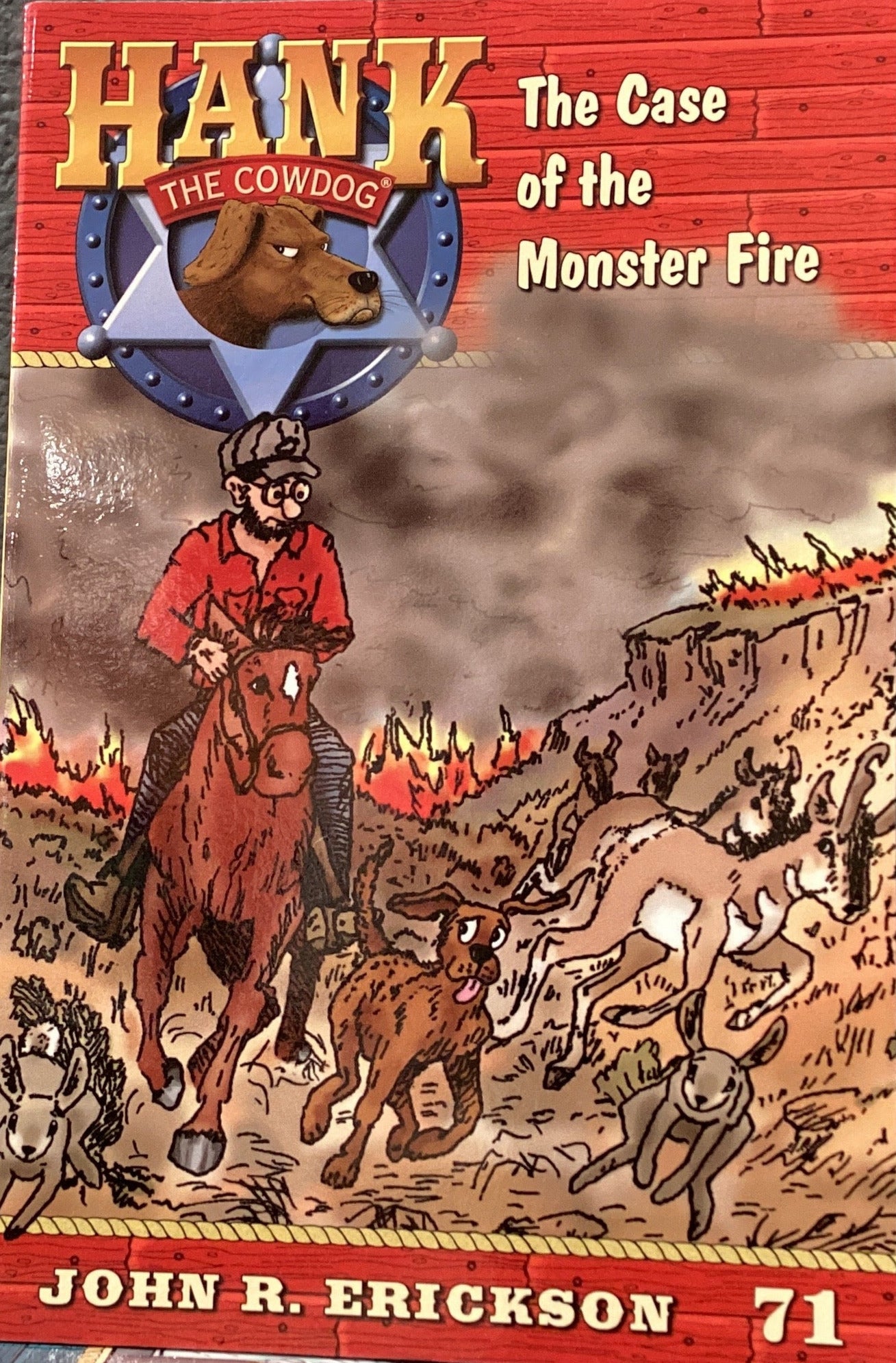 Book titled 'Hank the Cowdog: The Case of the Monster Fire' by John R. Erickson on a gray surface.