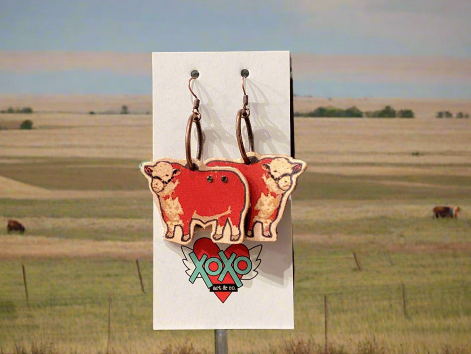 Pair of earrings with cow design on a card against a gray background