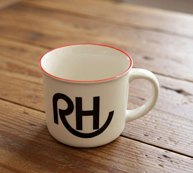 White mug with red rim and black initials on a wooden table