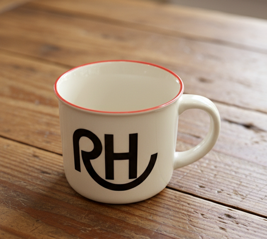 White mug with red rim and black initials on a wooden table