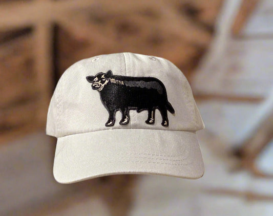 White cap with black Angus design on a beige surface against a gray wall