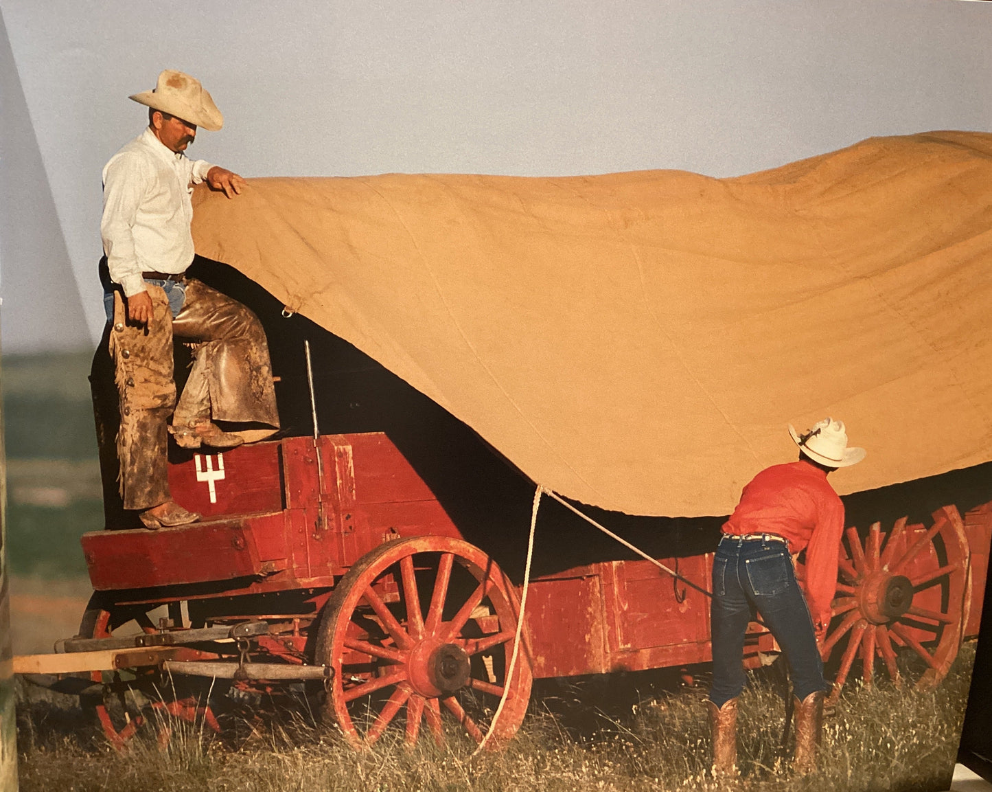 Two men with a red wagon and large brown blanket in an outdoor setting