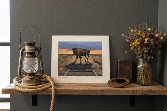 Two framed pictures of a bison on train tracks against a gray wall.