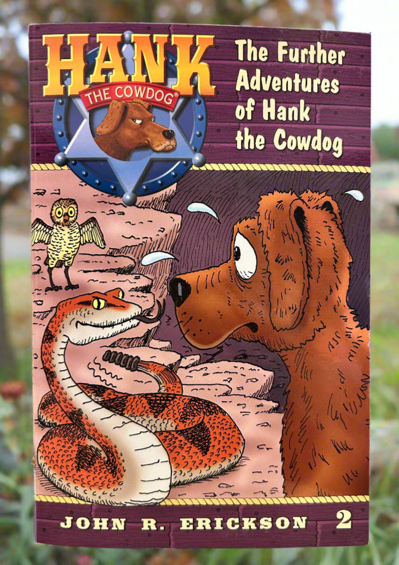 Book cover of 'The Further Adventures of Hank the Cowdog' by John R. Erickson on a wooden surface.