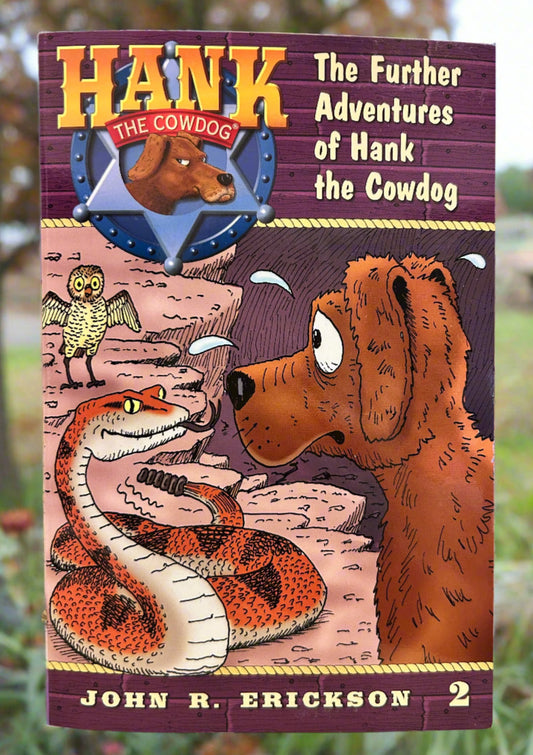 Book cover of 'The Further Adventures of Hank the Cowdog' by John R. Erickson on a wooden surface.