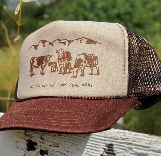 Trucker hat with cow design and text on a wooden post with a blurred green background