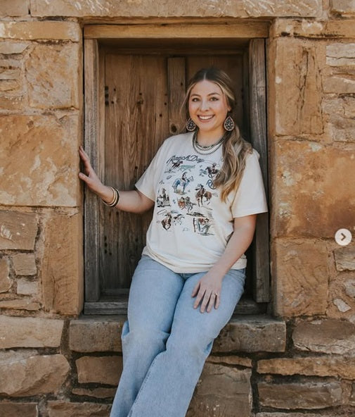Woman sitting in a rustic stone window frame wearing a graphic t-shirt and jeans.
