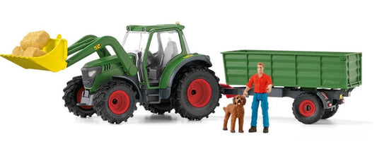 Toy tractor with front loader and trailer, accompanied by a figurine of a man and a dog on a white background.